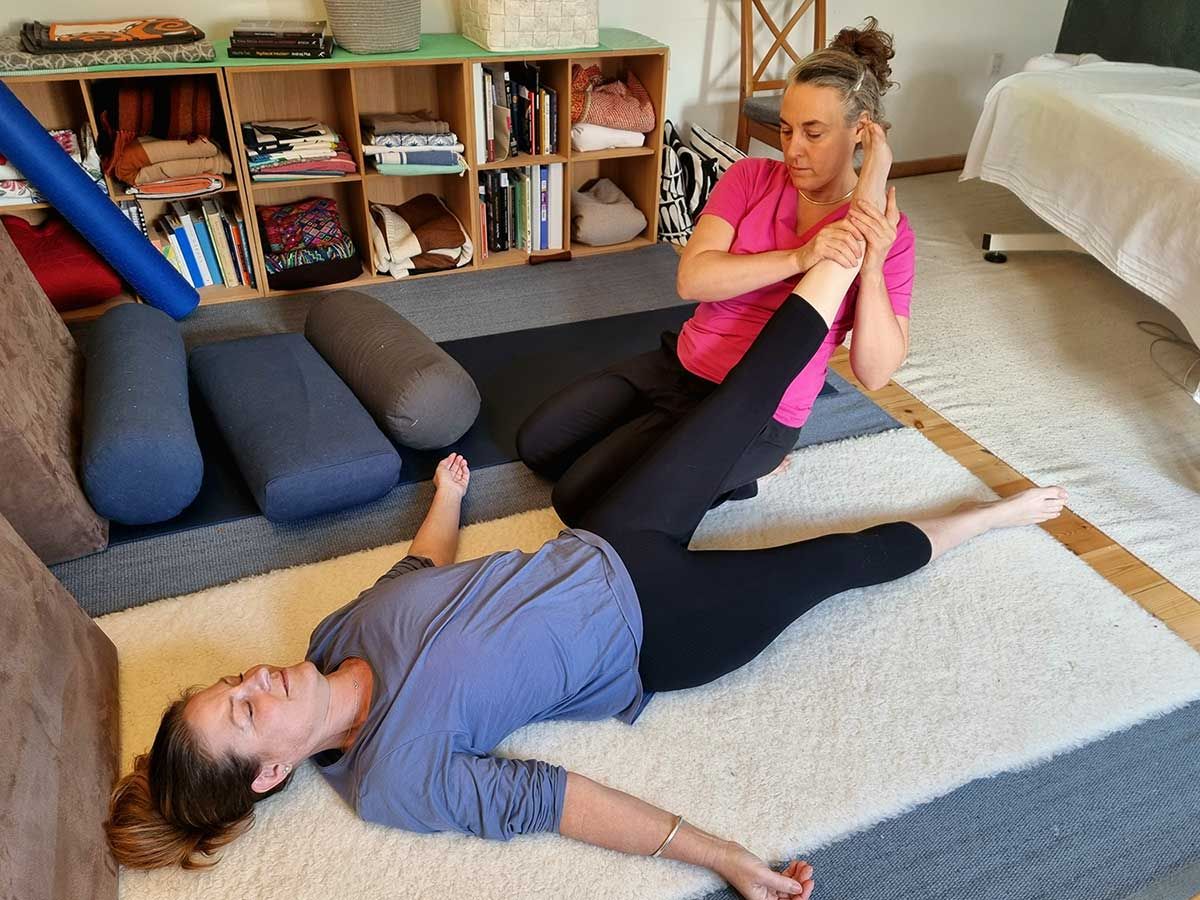 A woman is laying on the floor while another woman stretches her leg