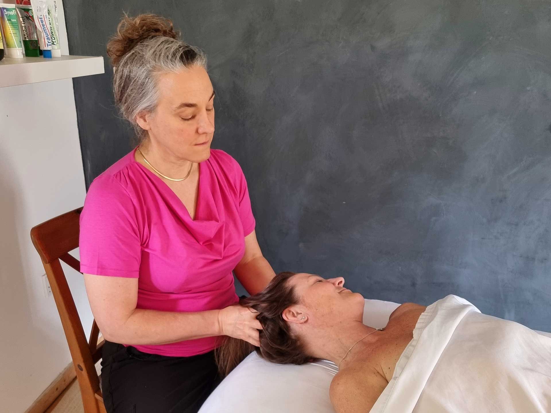 A woman in a pink shirt is giving a massage to a woman laying on a bed.