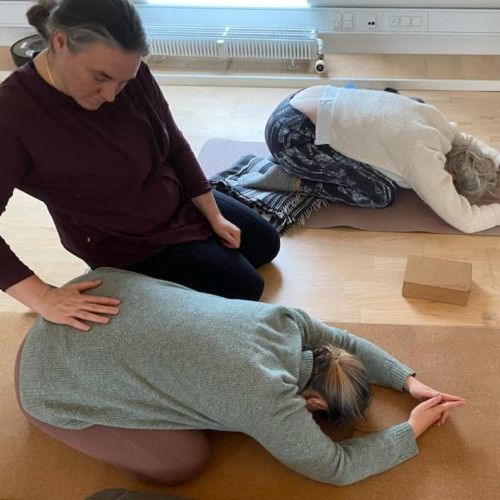 A woman is kneeling down next to another woman who is laying on a yoga mat.