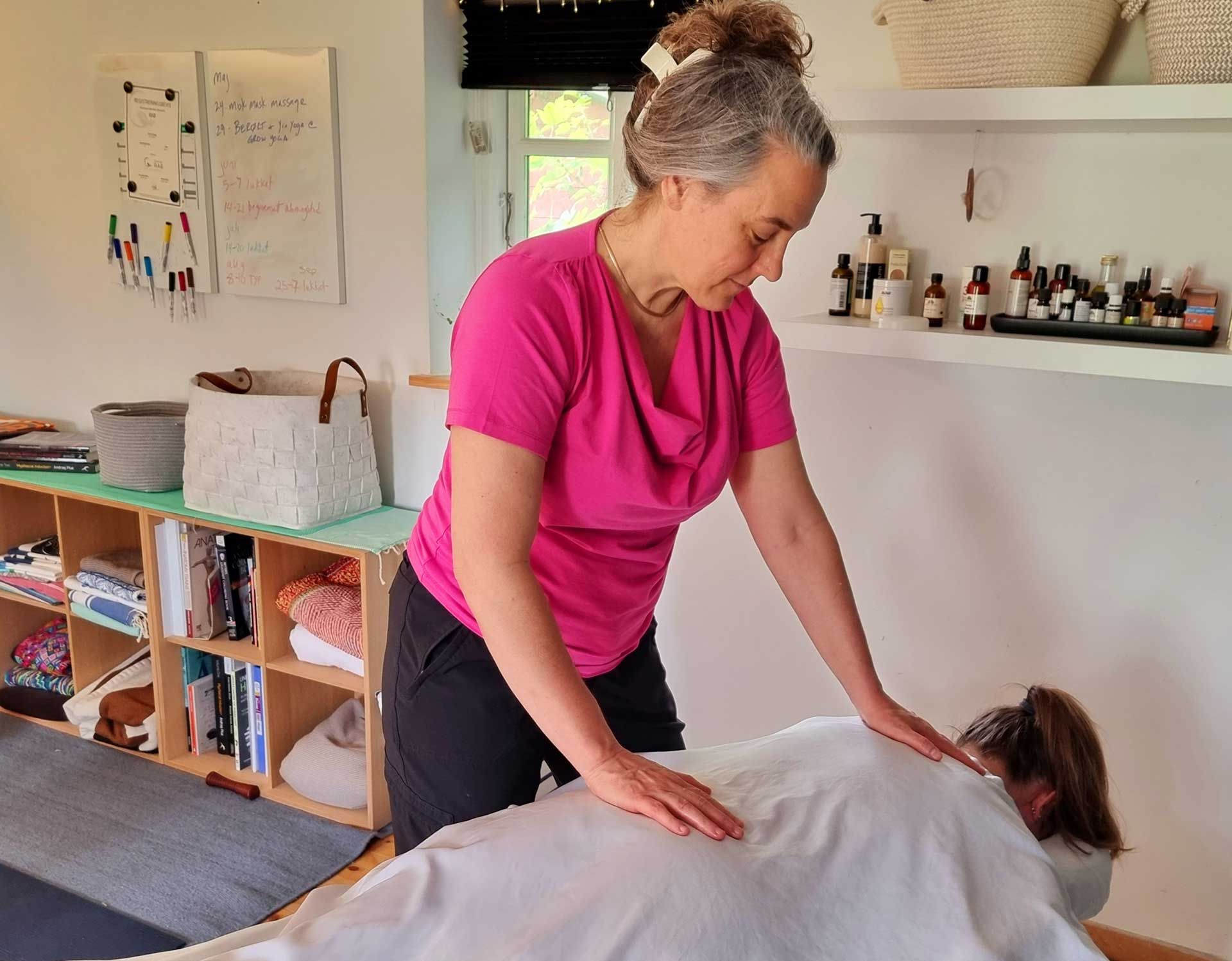 A woman in a pink shirt is giving a massage to a woman