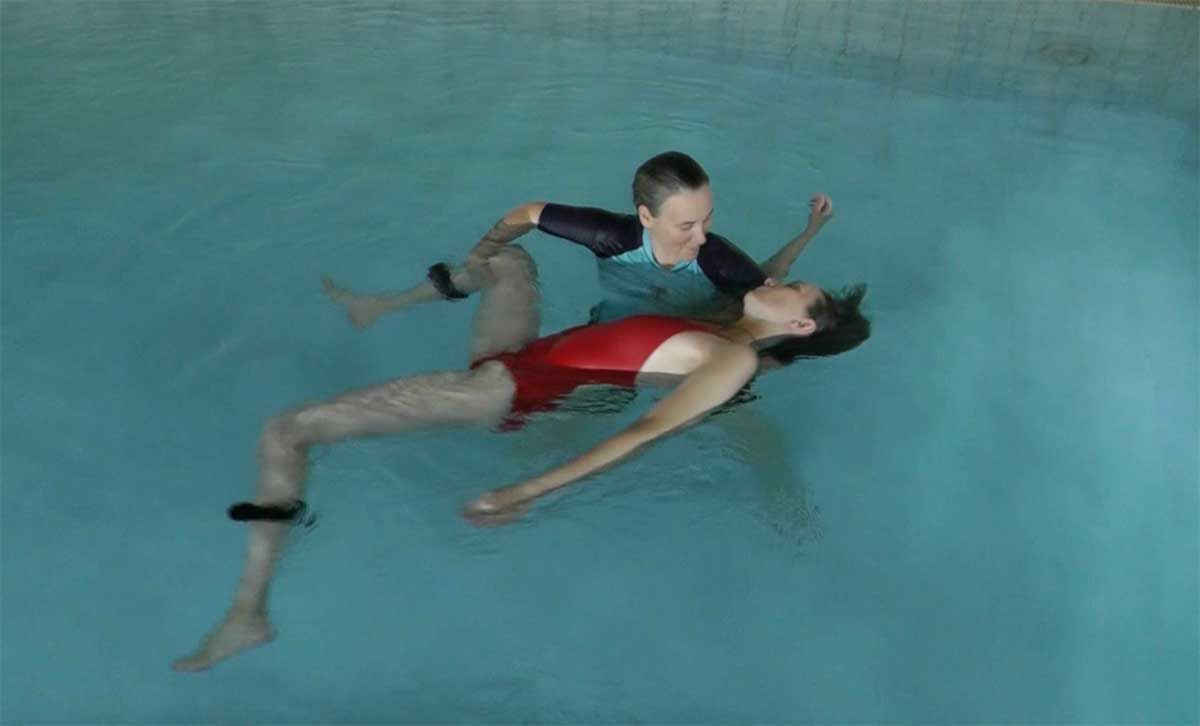 A boy is helping a woman float in a swimming pool.