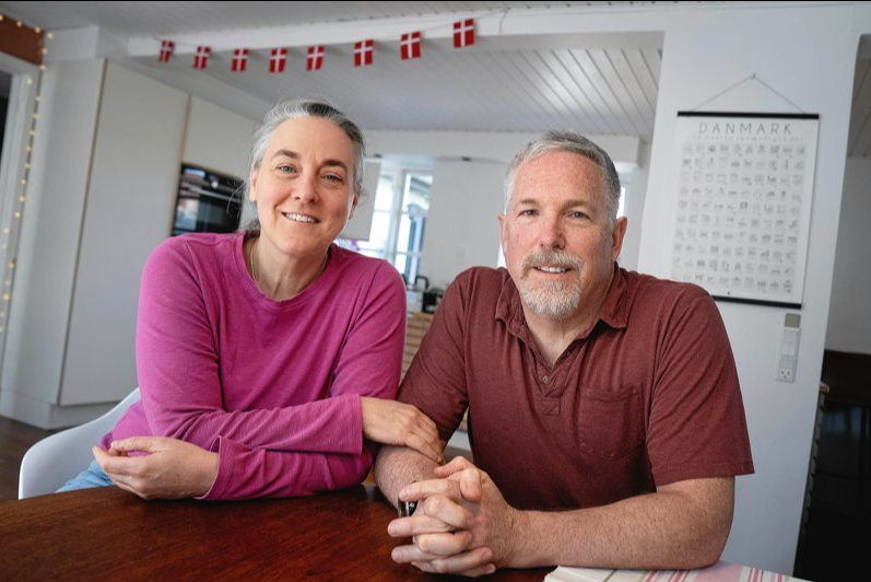 A man and a woman are sitting at a table with their hands folded