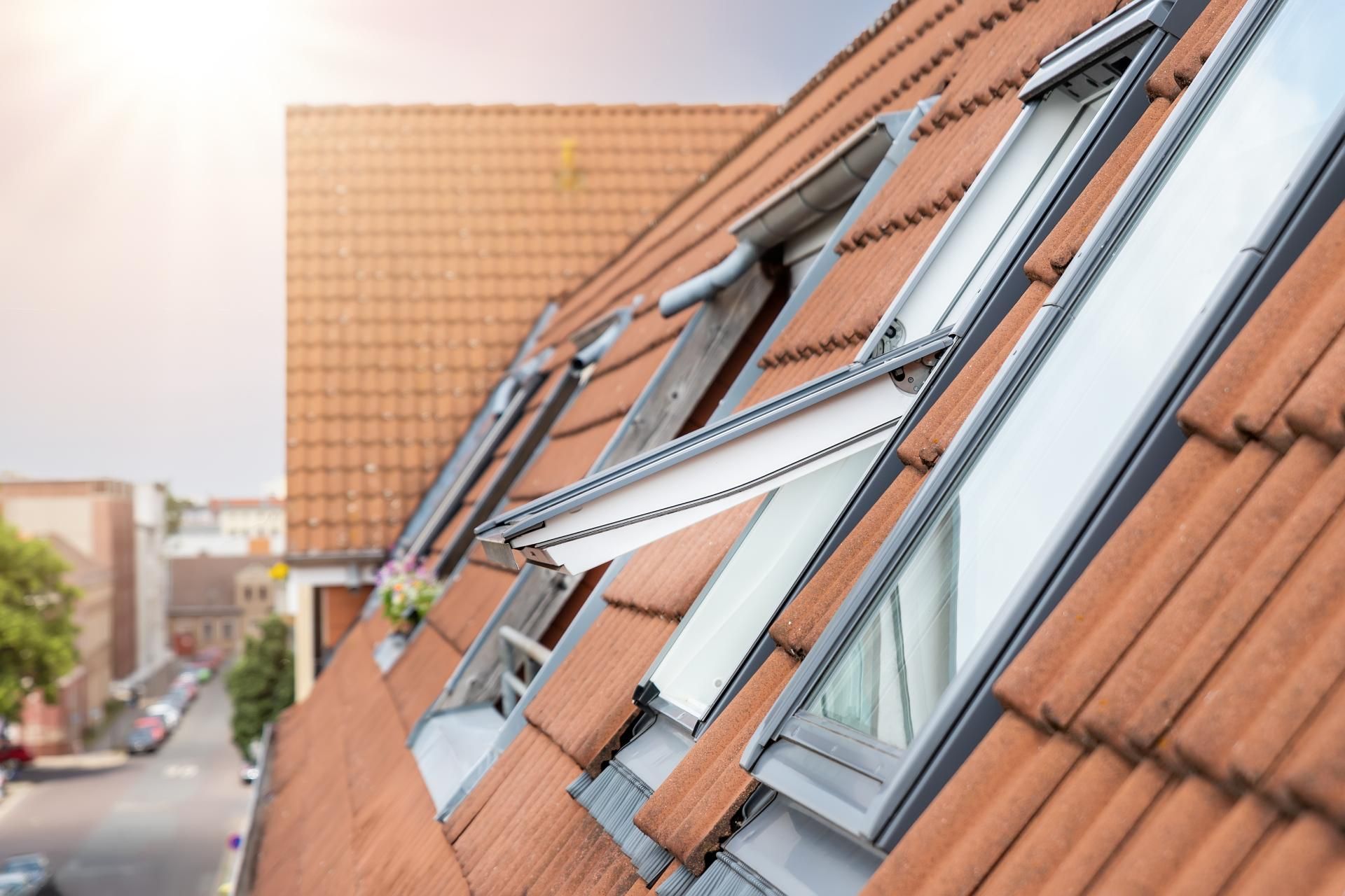 Angled view of a tiled roof with open skylight windows. City background in soft focus.