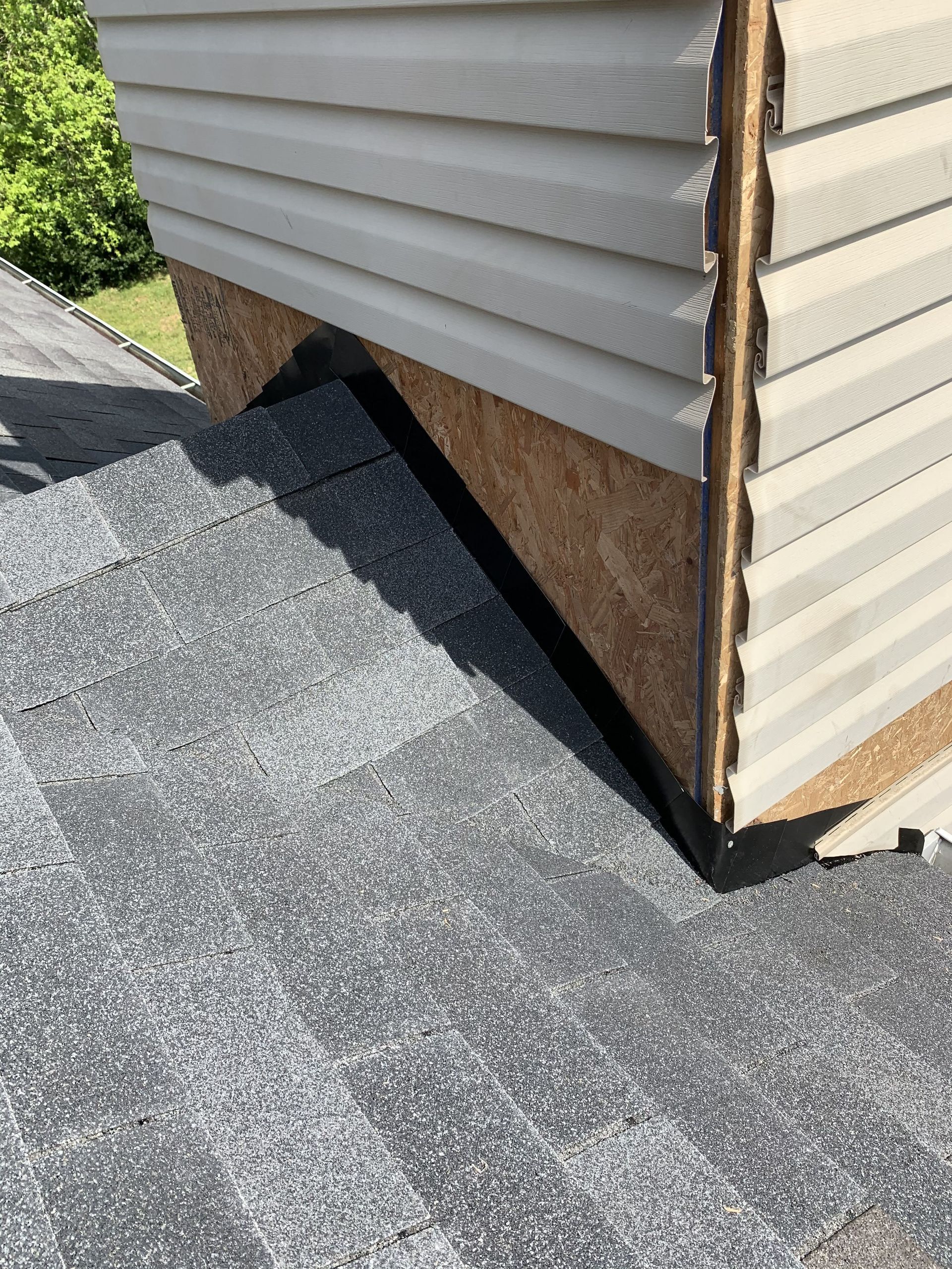 Close-up of a roof where the shingles meet a structure with siding. Brown wood is visible beneath the siding.