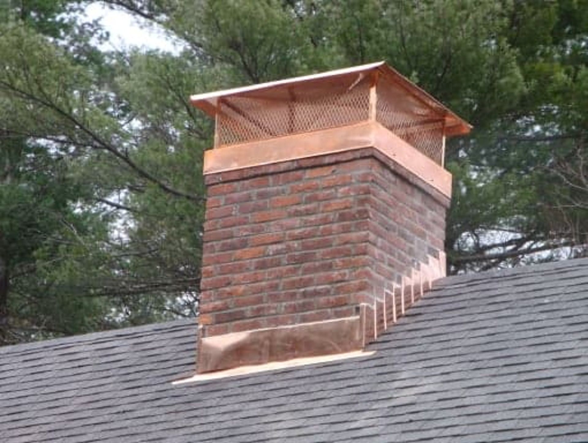 Brick chimney with copper cap and flashing on a dark shingle roof.