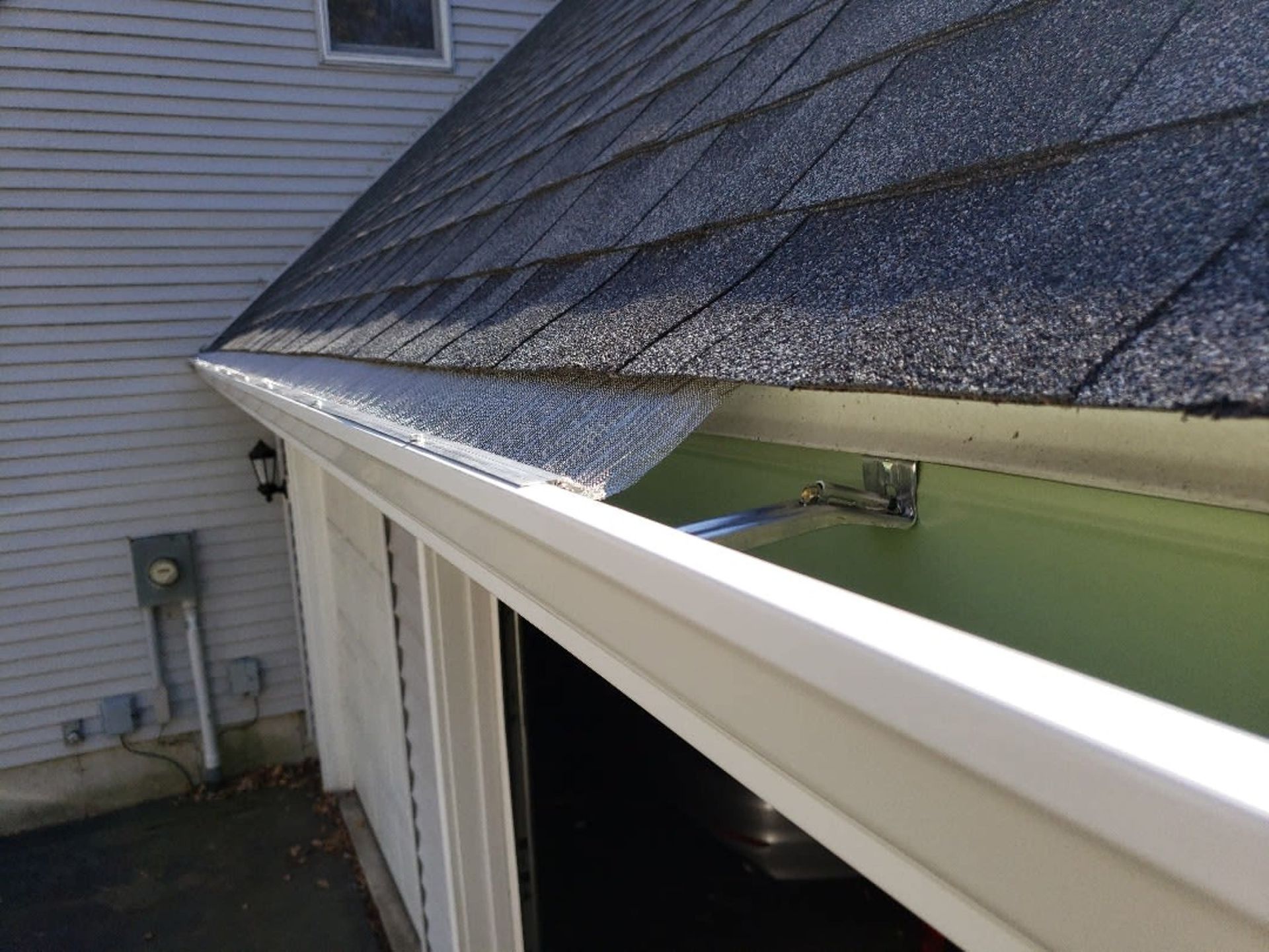 Gutter along a garage roof, with shingles above and a cream-colored frame.
