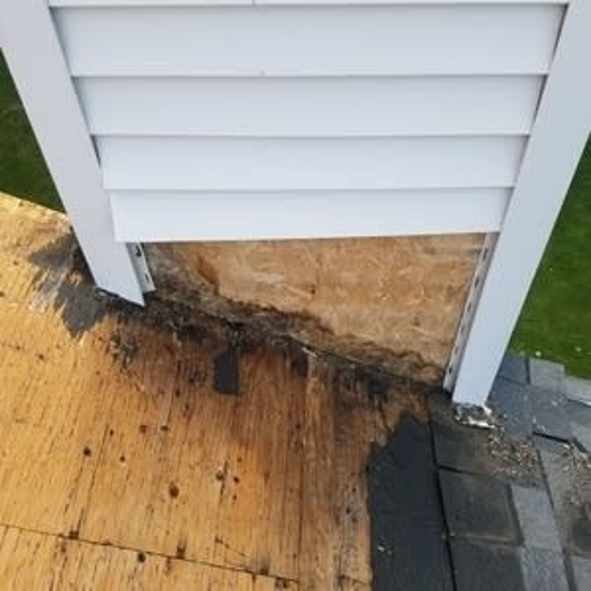 Damaged siding with rotted wood at the roof edge. White siding, visible wood, and black roofing.