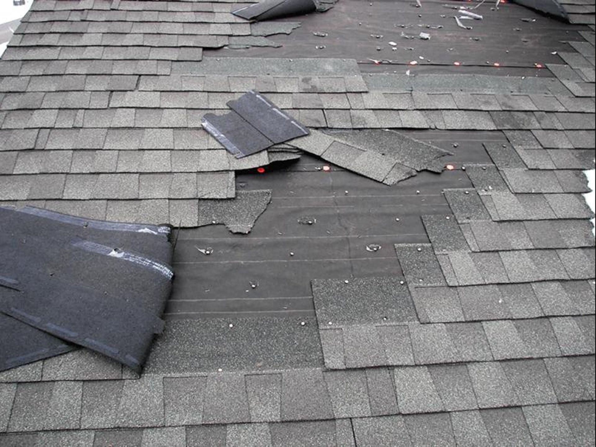 Damaged asphalt shingle roof with missing and torn shingles, exposing black underlayment.