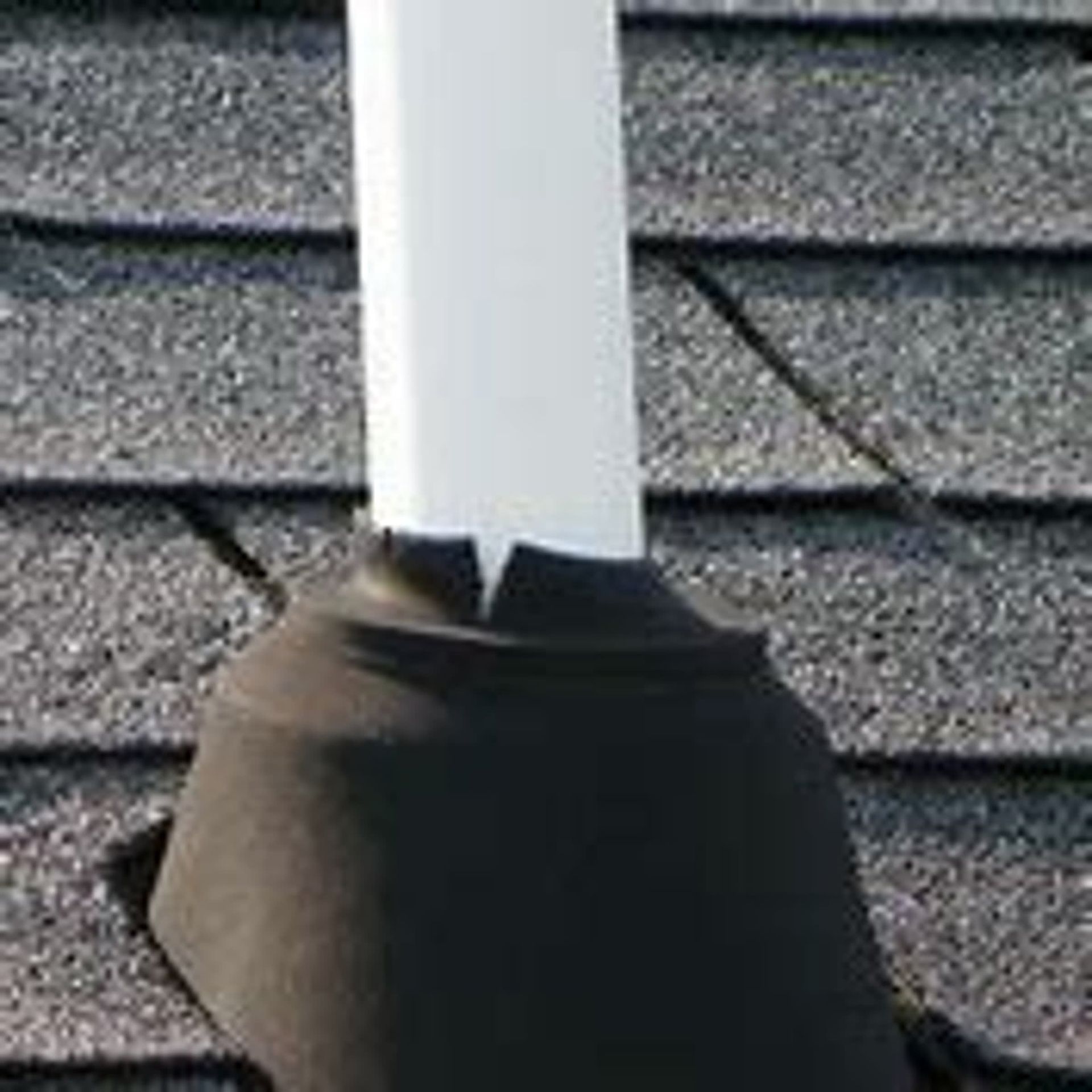 White pipe emerging from a black rubber roof flashing on a gray shingle roof.