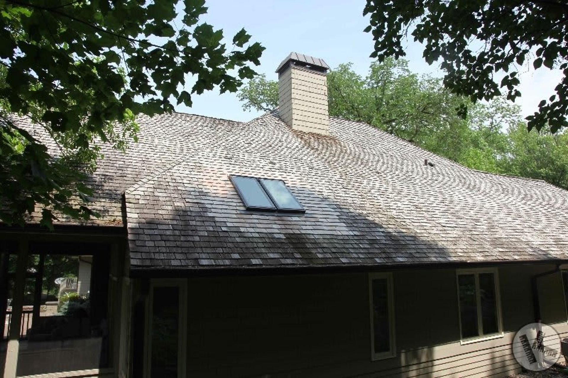 Wood shingle roof with a chimney and skylight, surrounded by trees.