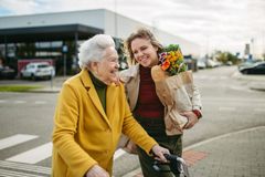 A woman is helping an elderly woman with a walker cross the street.