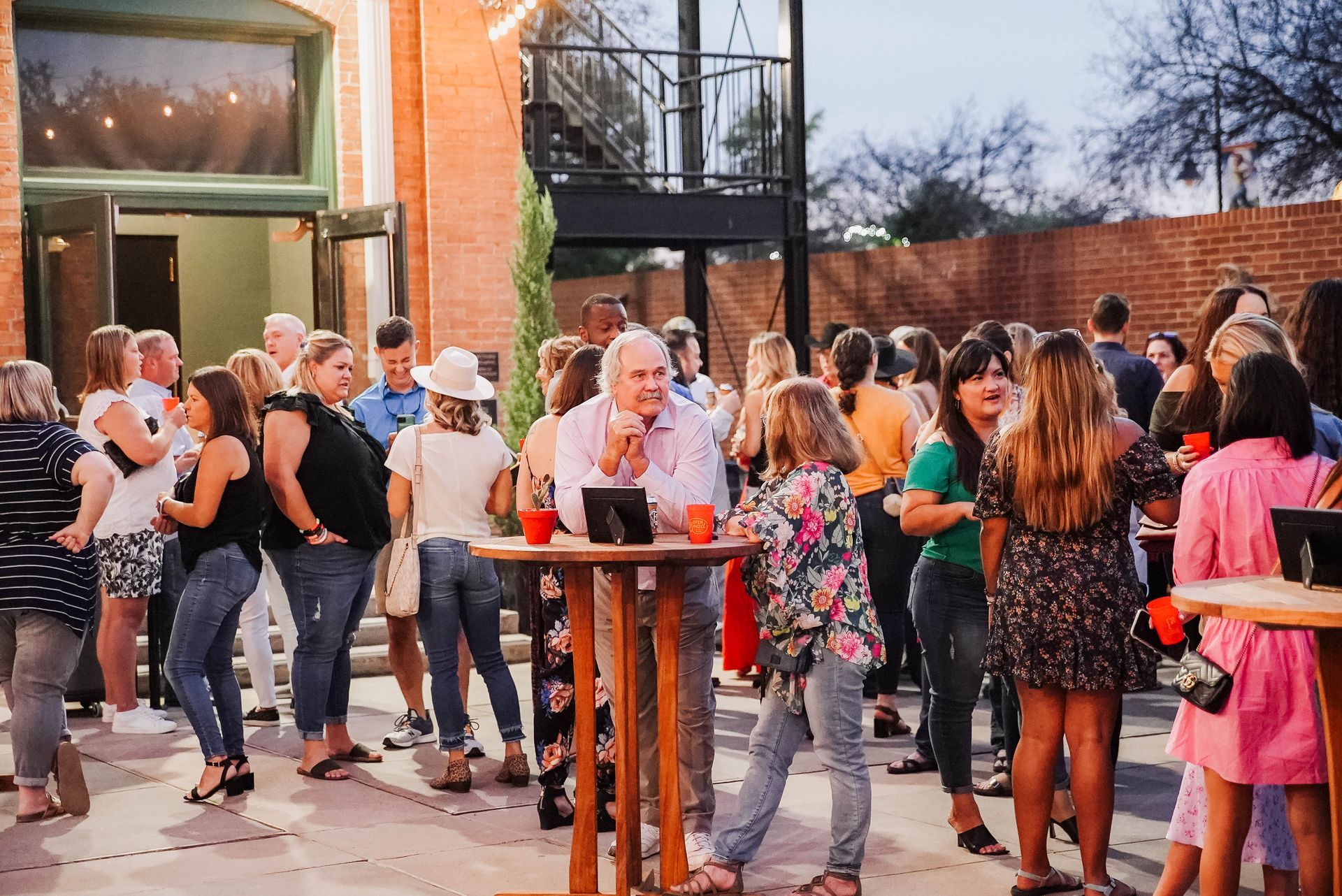 A large group of people are standing around tables outside of a building.