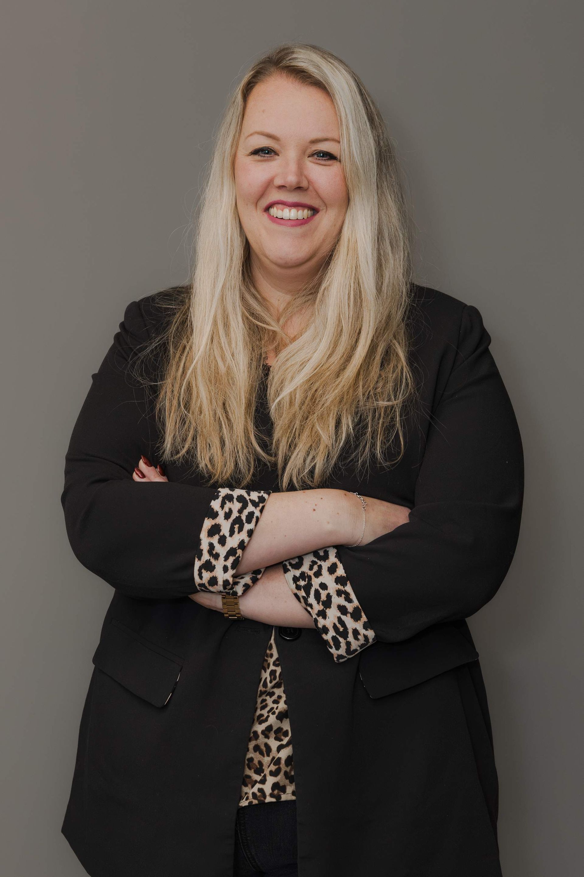 Een vrouw glimlacht aan een tafel, met een klein kopje in haar hand, in een restaurant met donkere interieurs.