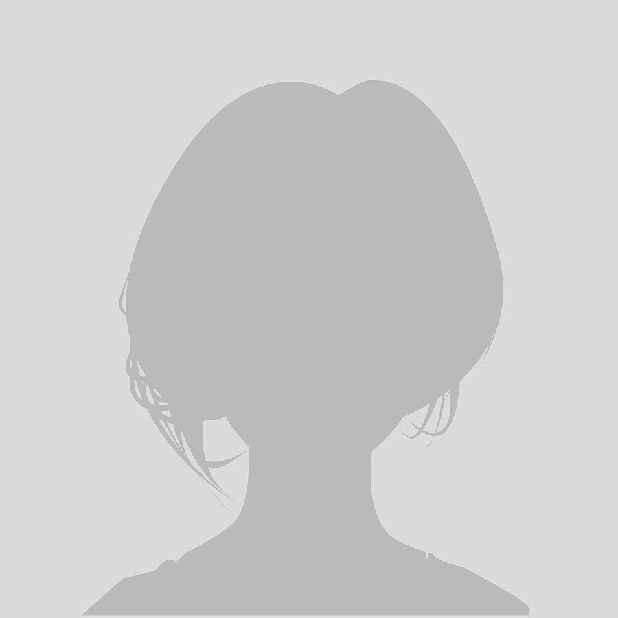 Vrouw met blond haar, armen omhoog, lachend, gekleed in een zwarte blazer met manchetten en blouse met luipaardprint.