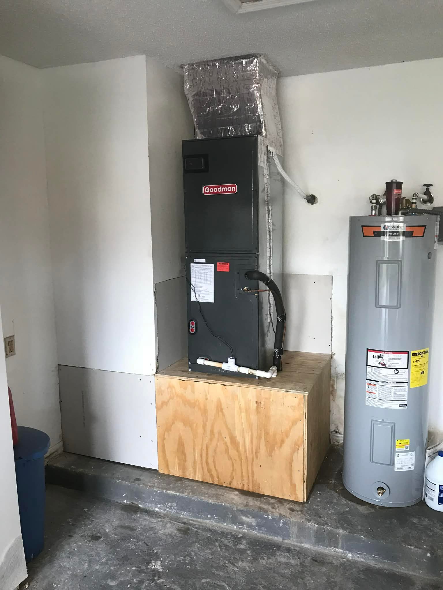 Black furnace on wood platform beside gray water heater in a garage utility room.