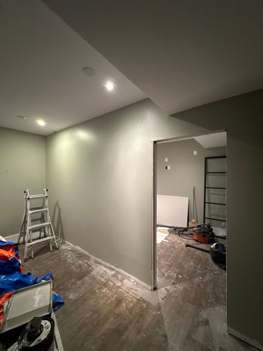 Renovated room with gray walls, recessed lights, ladders, and construction debris on the floor