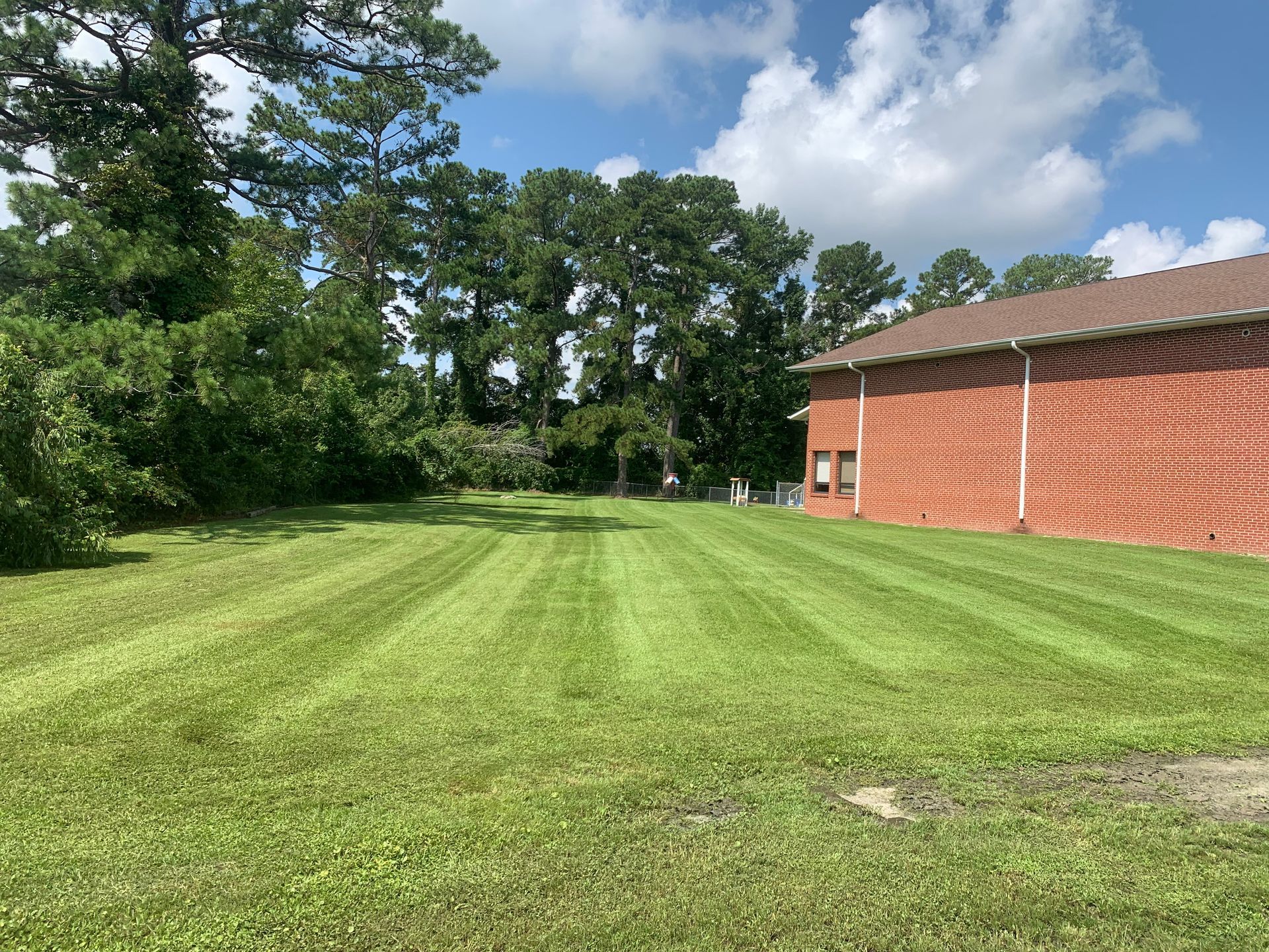 A lush green lawn in front of a brick building with trees in the background.