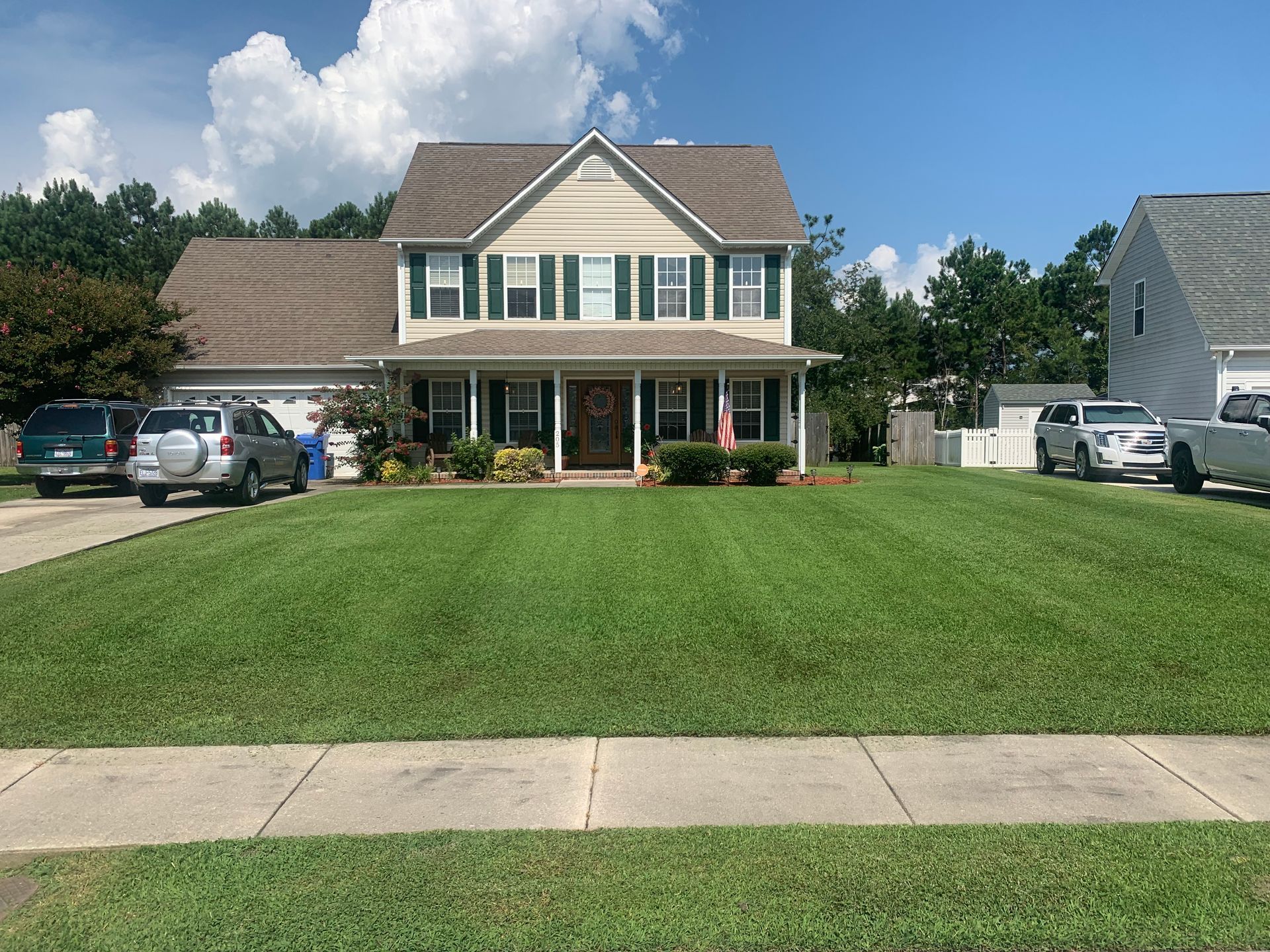 A house with a lush green lawn and cars parked in front of it