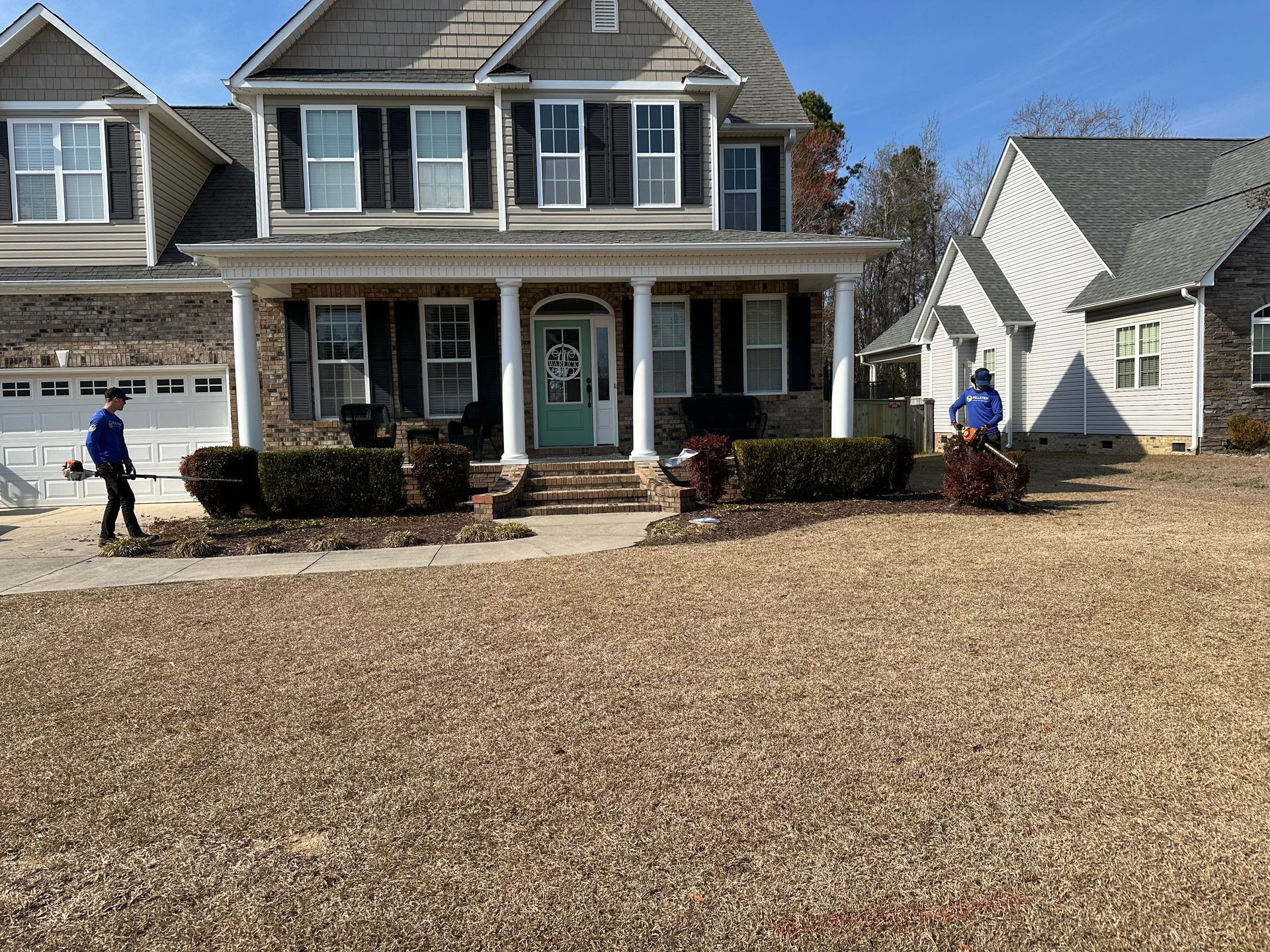 A man is riding a lawn mower in front of a large house.