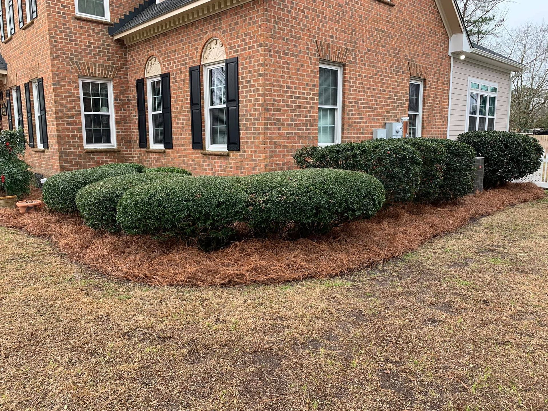 A brick house with black shutters and bushes in front of it.