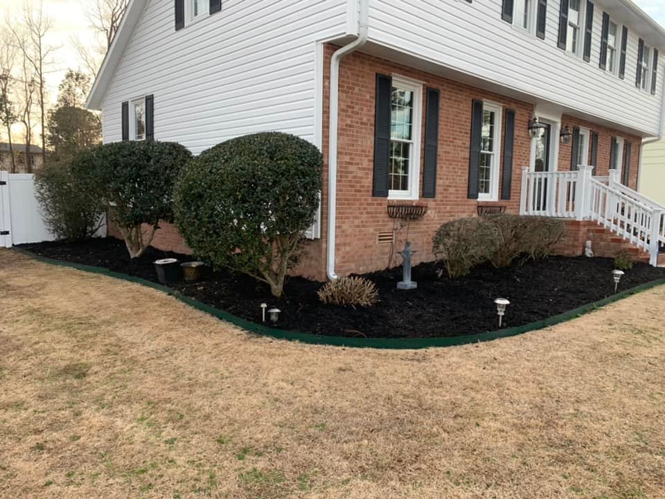 A brick house with black mulch edging the house & manicured small trees