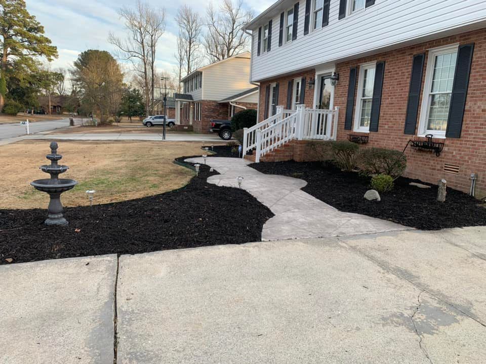 A brick house with a walkway and a fountain in front of it and black mulch.