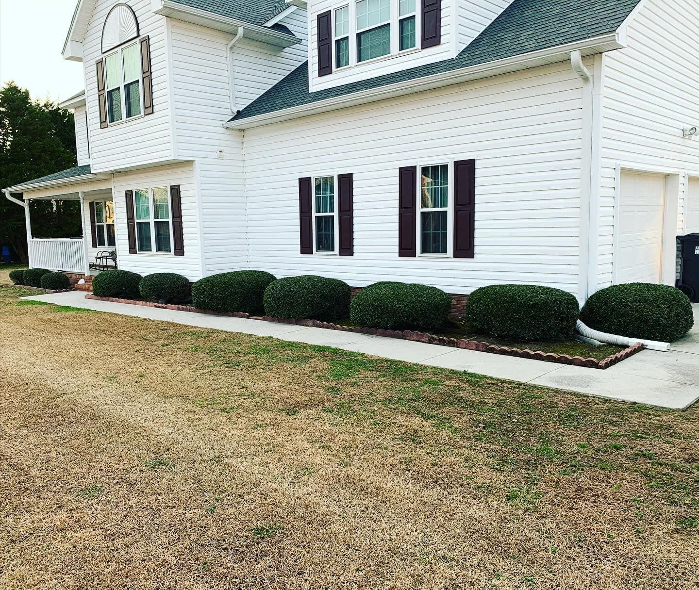 A white house with black shutters and bushes in front of it.
