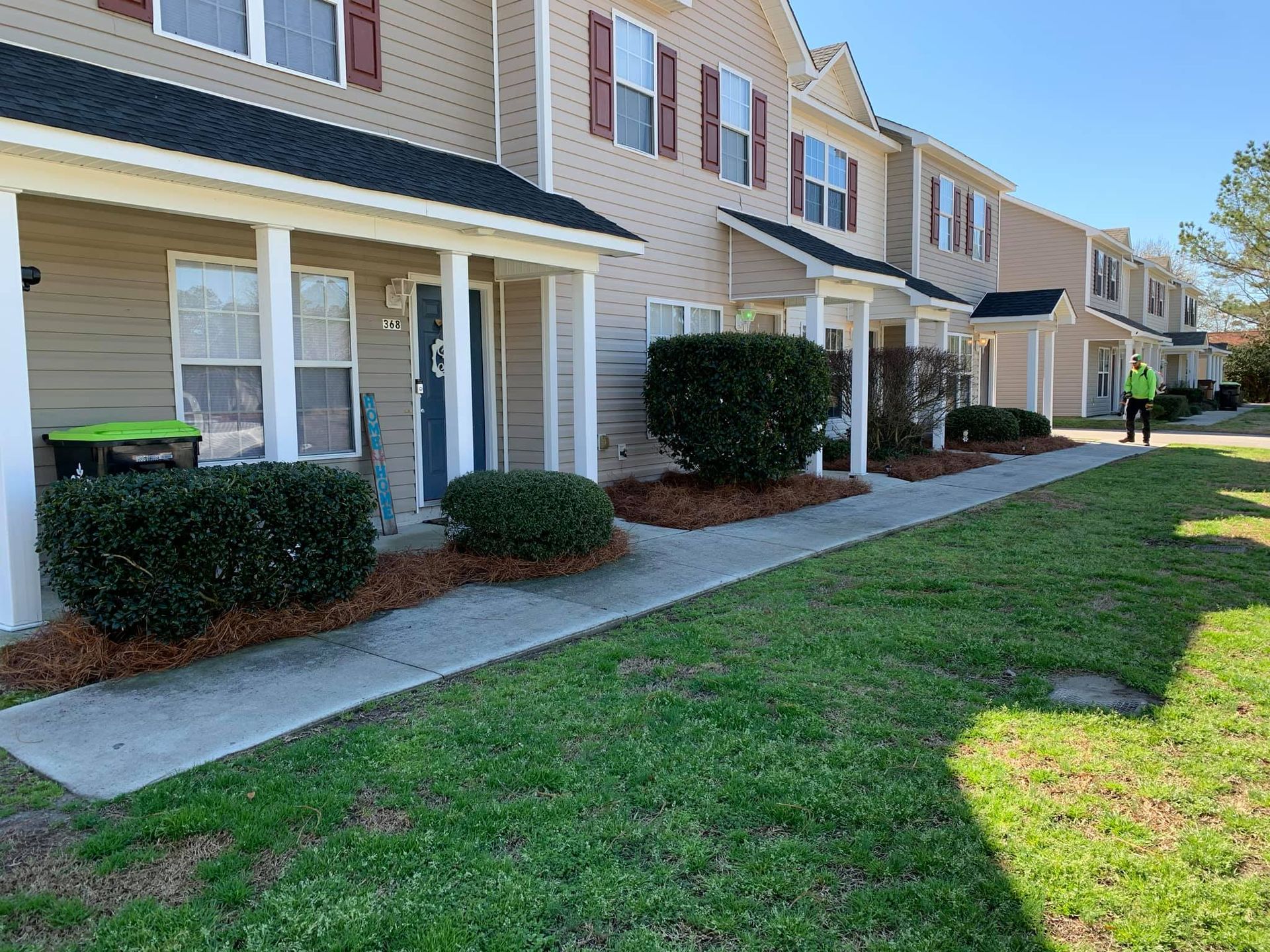 Apartment buildings with pine straw and trimmed bushes and trees.