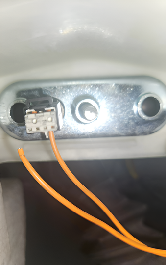 A close-up of a metal plate with three holes, showing a black electrical connector with two loose orange wires.