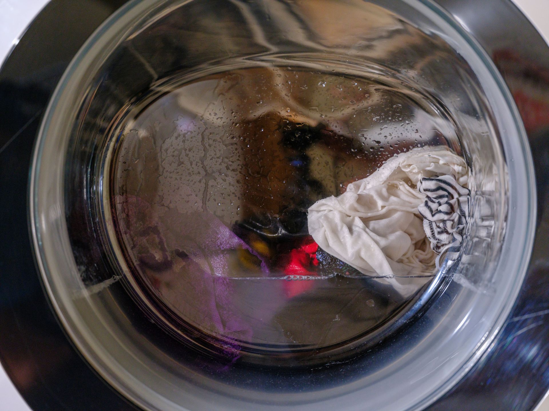 Washing machine drum with a white garment and a purple item inside, seen through the door