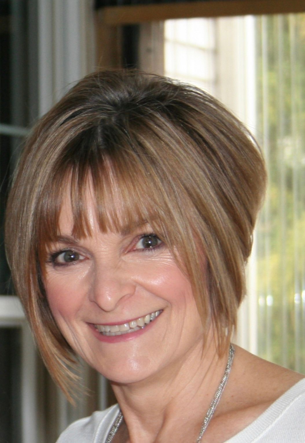 A woman with short brown hair is smiling and wearing a white shirt.