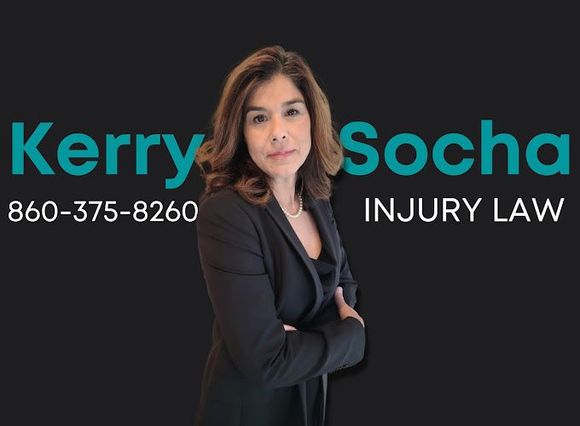 A woman is standing with her arms crossed in front of a sign for kerry socha injury law.