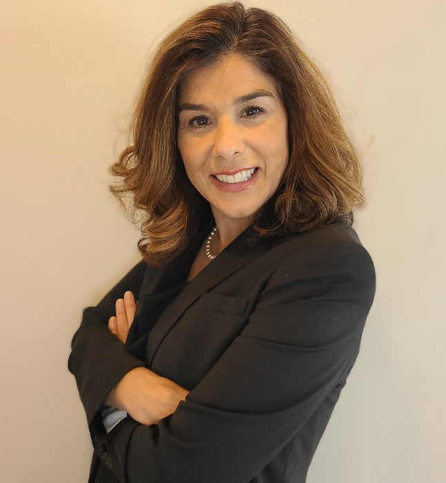 A woman in a black suit is smiling with her arms crossed