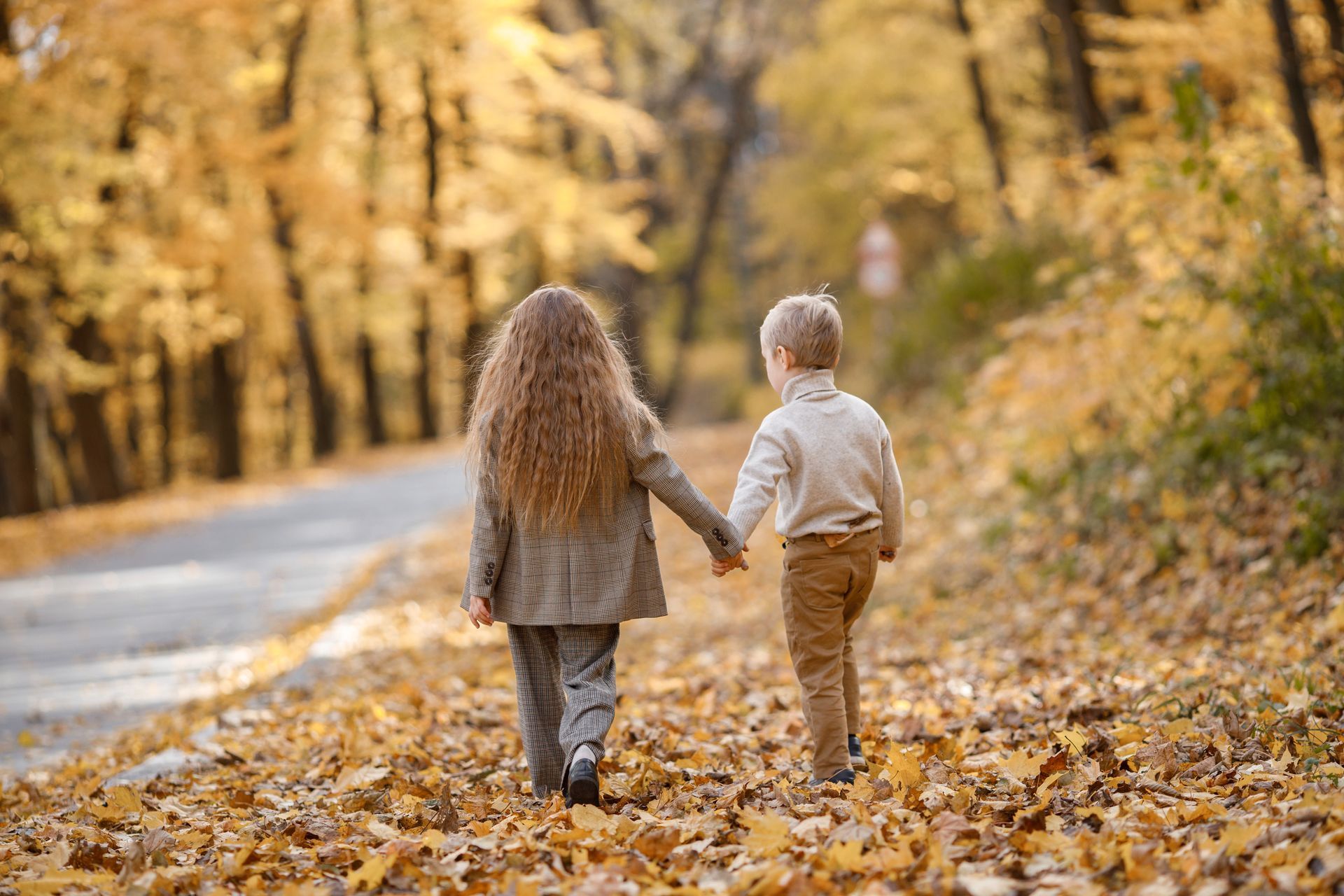A boy and a girl are walking down a road holding hands.