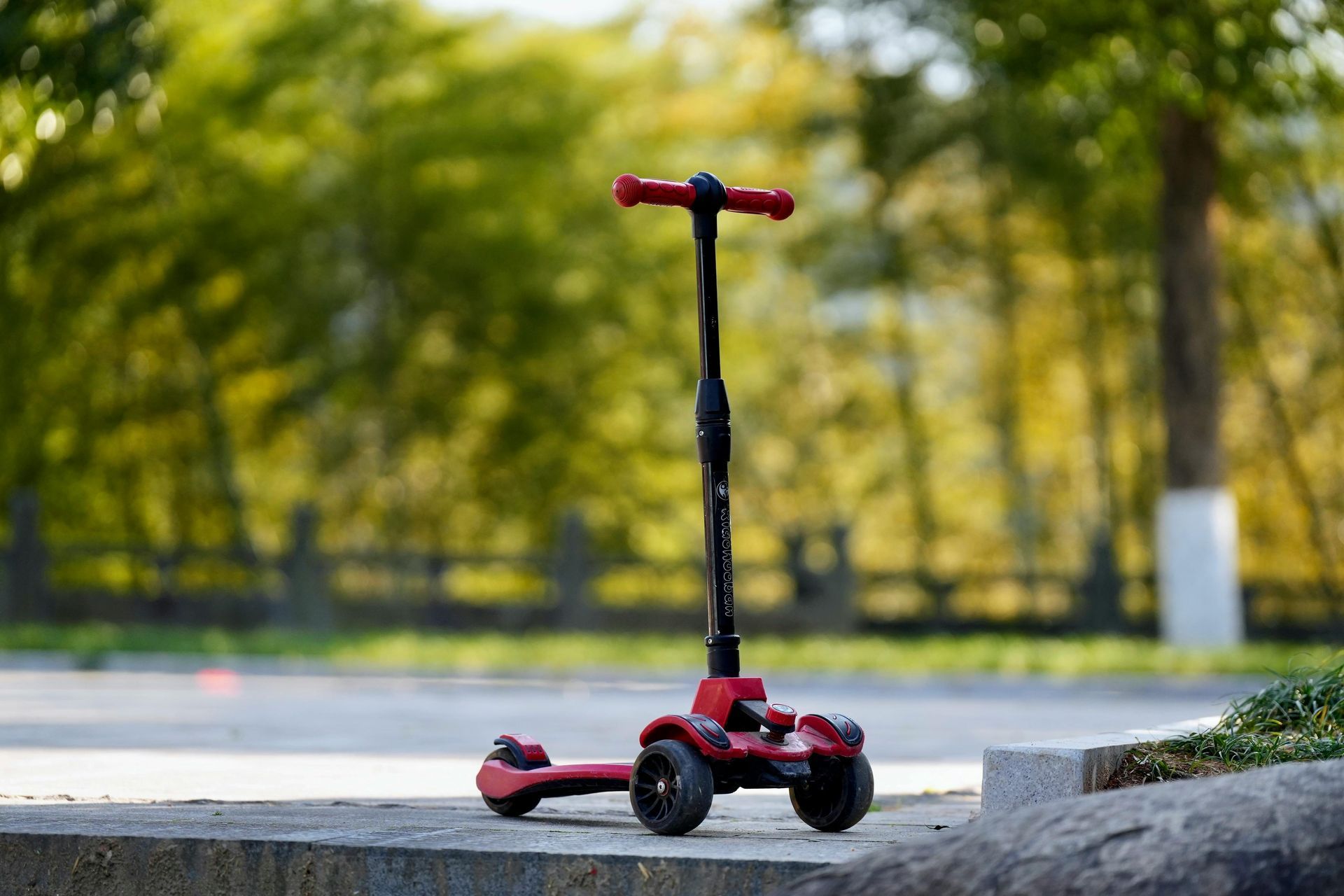 A red scooter is sitting on a sidewalk in a park.