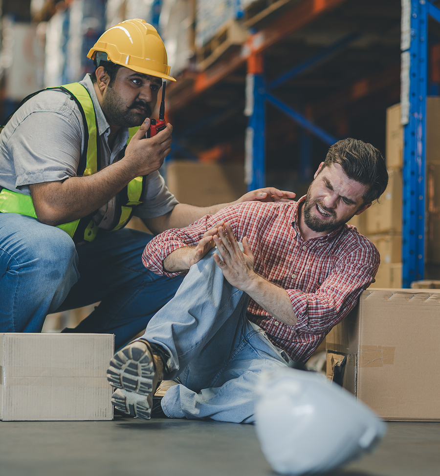 A man in a hard hat is helping another man who has fallen in a warehouse.