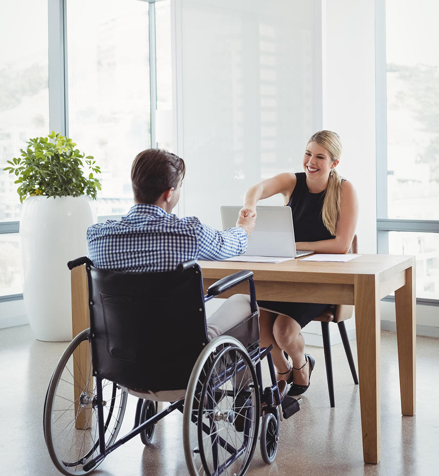 A man in a wheelchair is shaking hands with a woman at a table.