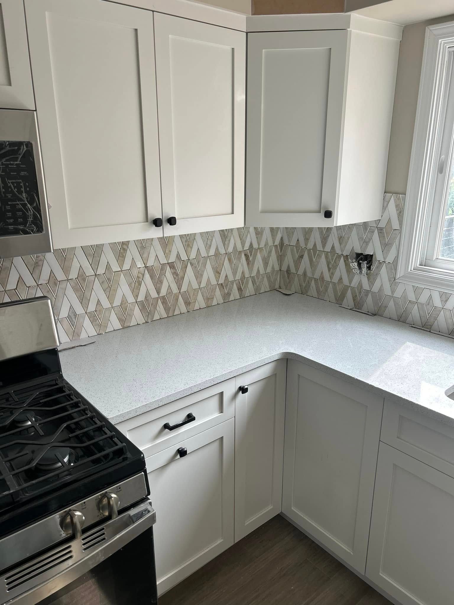 White kitchen cabinets with gray countertops and patterned backsplash.
