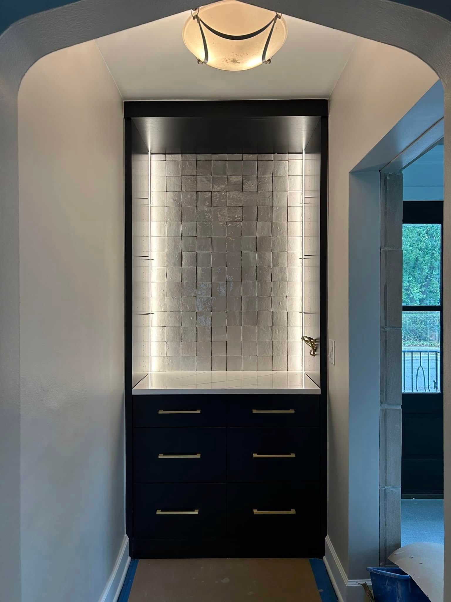 Built-in navy cabinet with drawers and countertop in a hallway, lit by an overhead fixture and vertical lights.