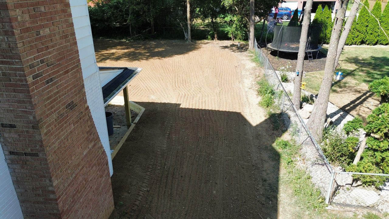 An overhead view of a backyard showing a newly laid lawn patch next to a brick house and a trampoline in the distance.