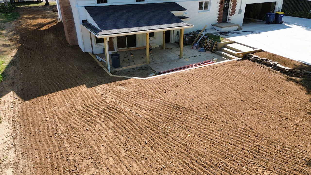 An aerial view of a freshly tilled, dirt backyard next to a house with a covered porch and stone stairs.