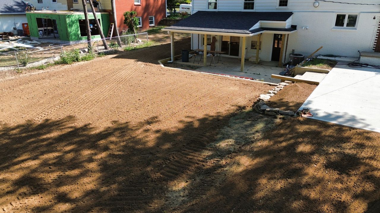 An elevated view of a backyard featuring a brown dirt lawn, a new patio cover, and a fresh concrete walkway.