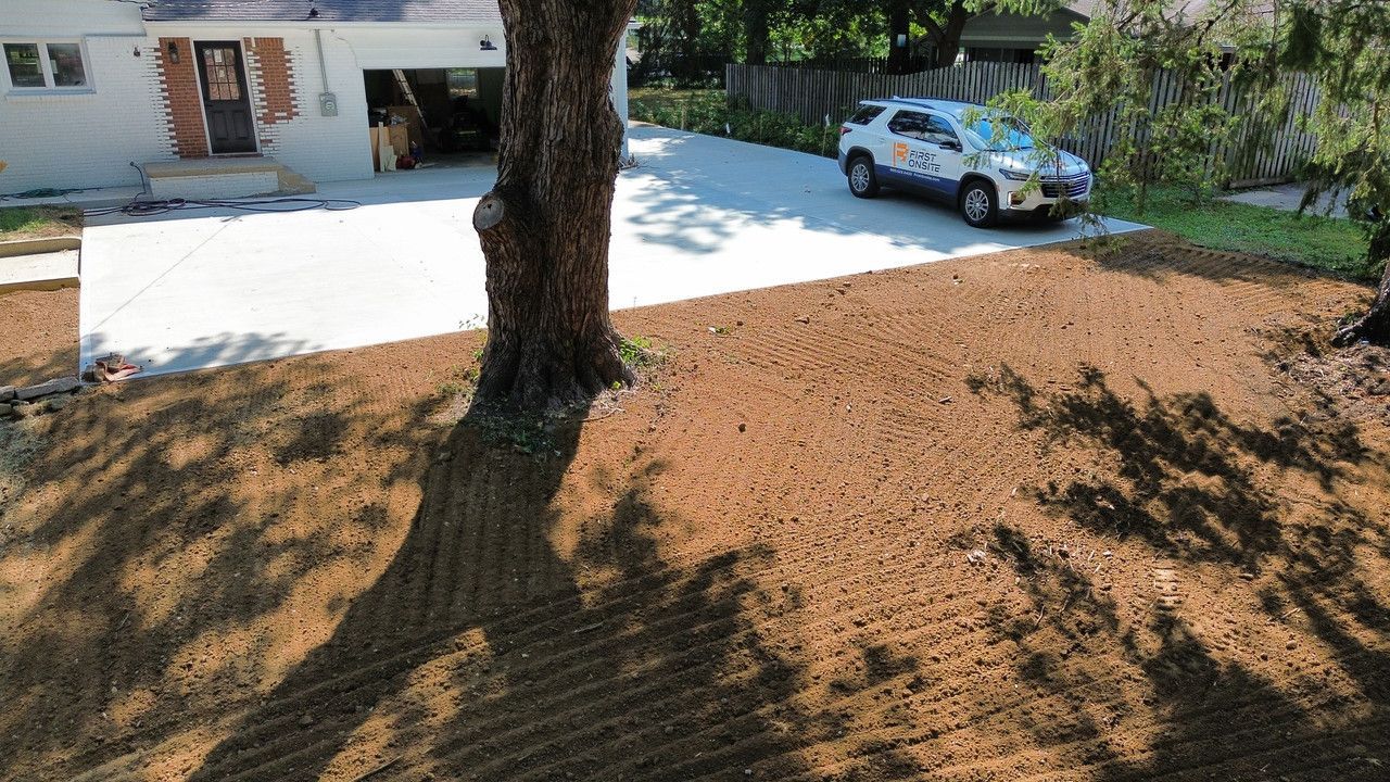 A freshly tilled brown yard sits in front of a house with a new concrete driveway and a parked SUV.