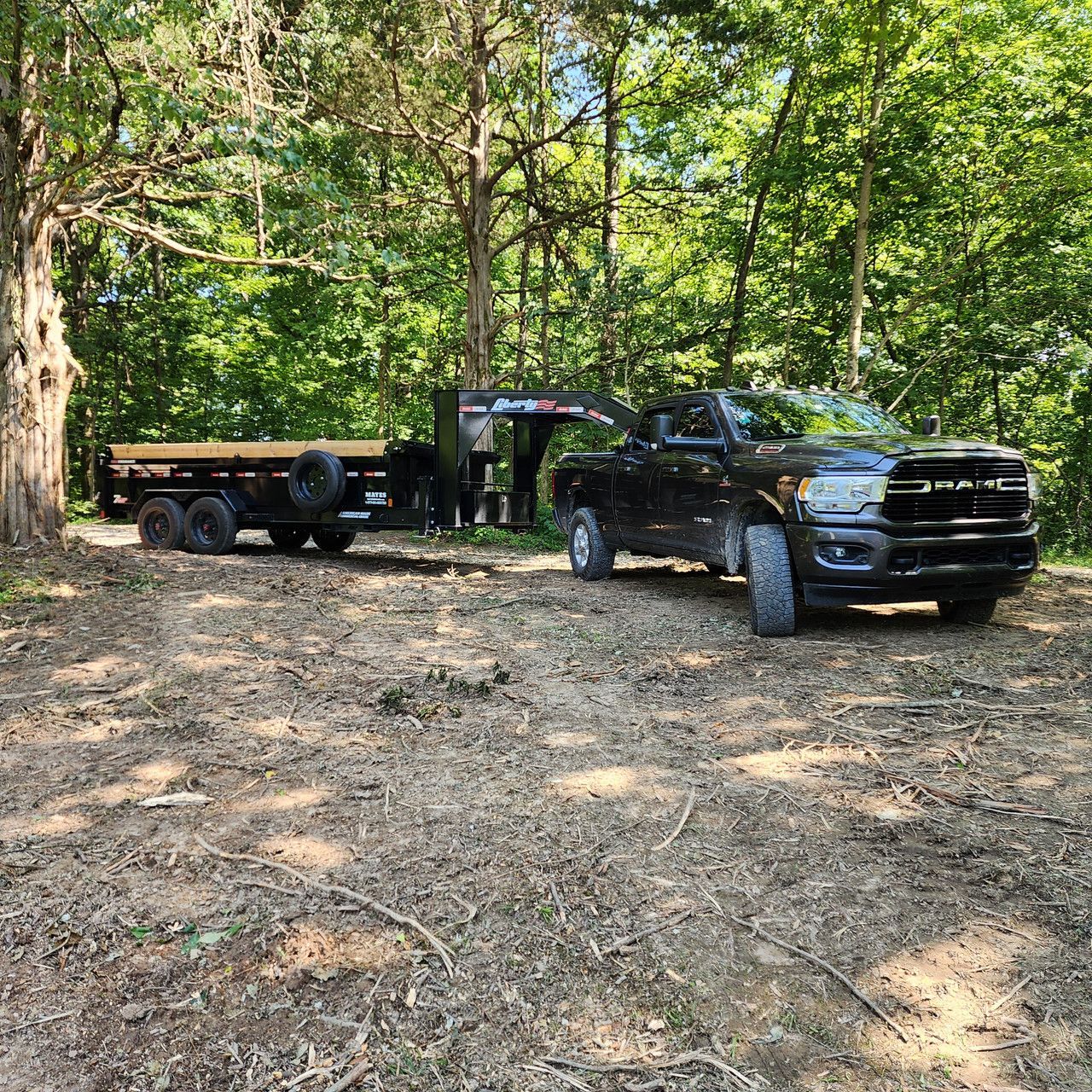 A black Ram pickup truck pulling a black gooseneck dump trailer parked in a wooded area.