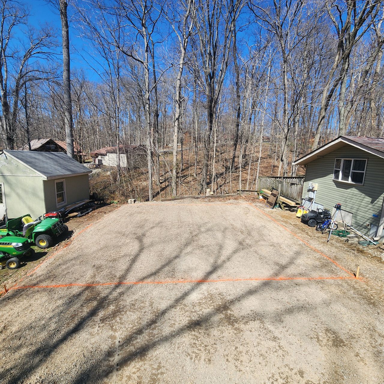 A gravel plot between two small sheds on a wooded property with an orange string line marking a rectangular area.