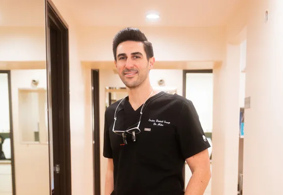 Dr. Mamaliger in a black scrub top and glasses is standing in a hallway.