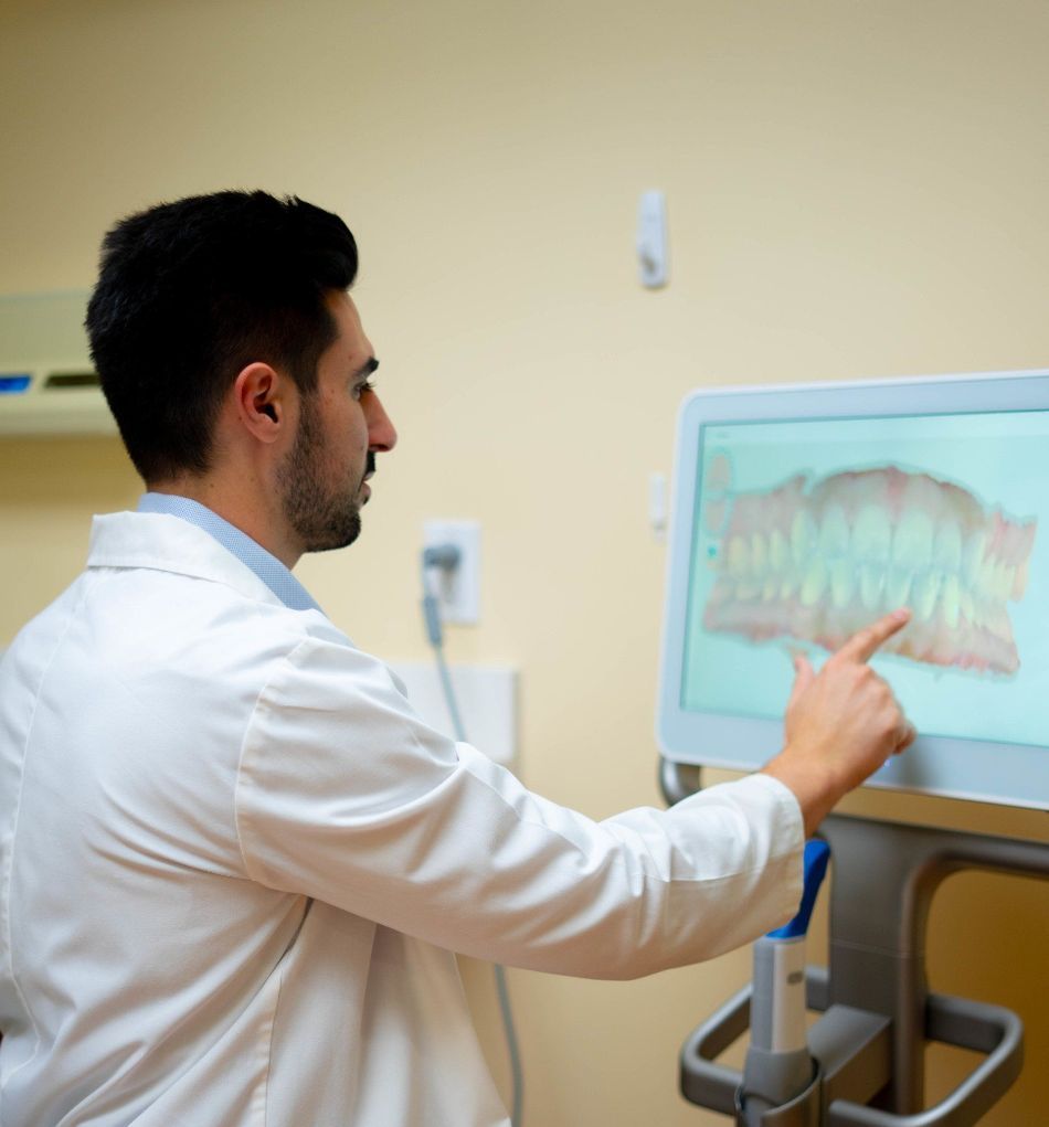 Dr. Mamaliger  in a lab coat is pointing at a screen with a picture of teeth on it