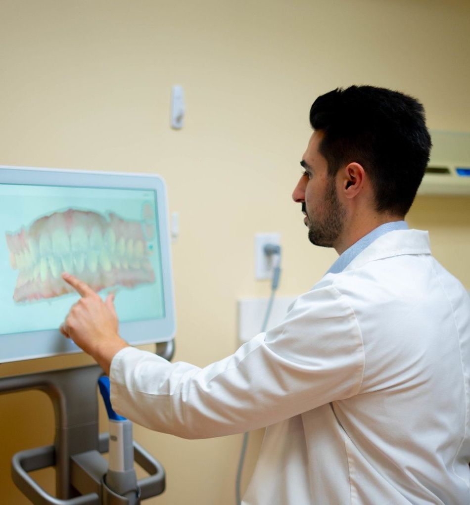 Dr. Mamaliger  in a lab coat is pointing at a screen with a picture of teeth on it