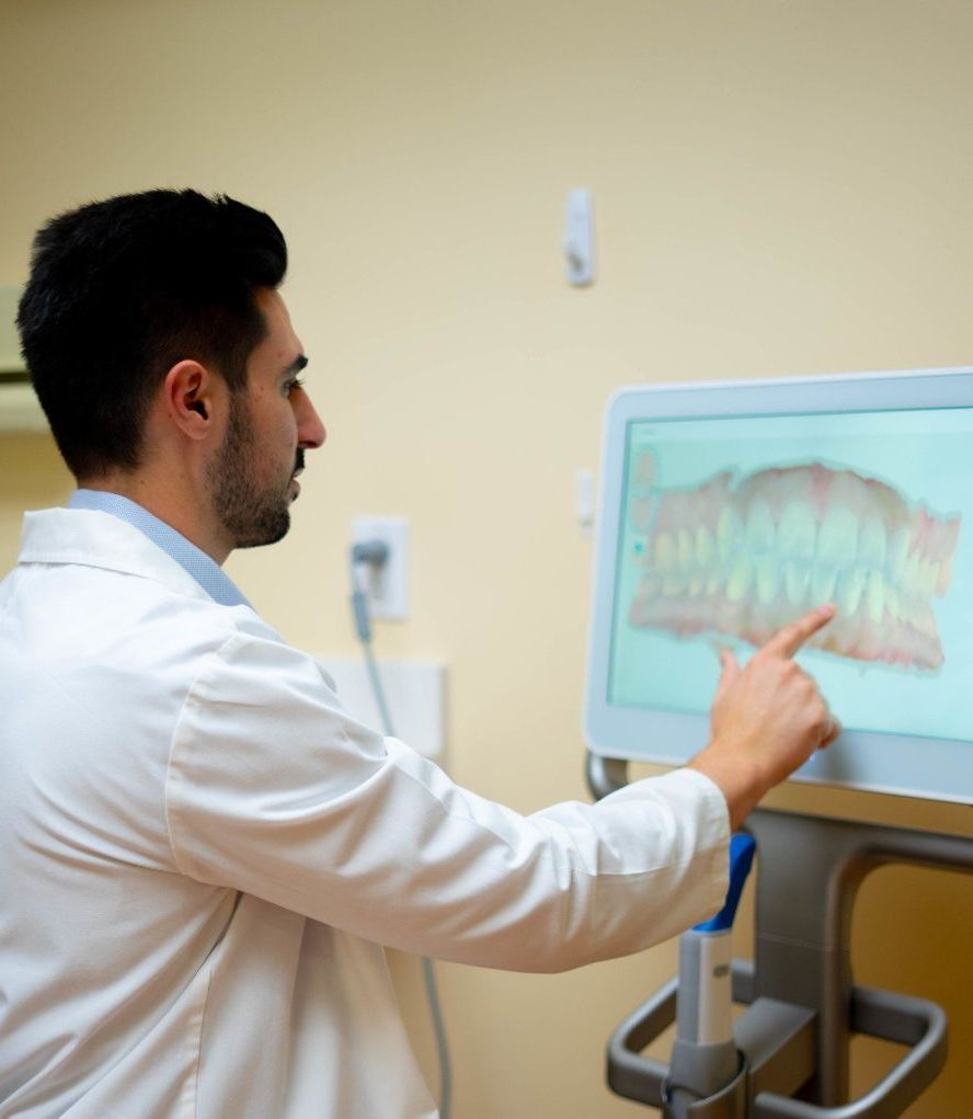 Dr. Mamaliger  in a lab coat is pointing at a screen with a picture of teeth on it