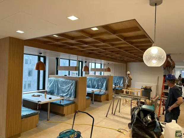 Modern office interior under construction with desks, wood paneling, plastic-covered partitions, and a hanging light